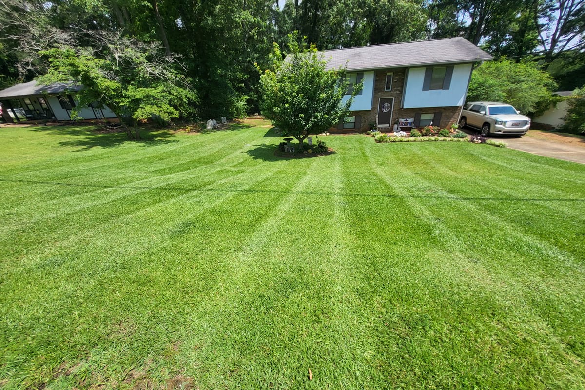 A front lawn freshly mown in wide stripes, with clean edges along the beds